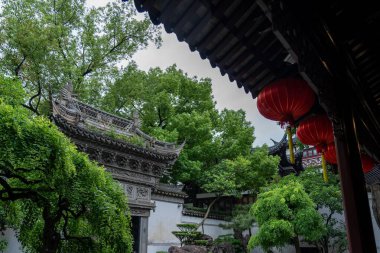 Şangay, Çin - Haziran 06, 2024: Çin 'in Şangay kentindeki Yu Garden manzarası, geleneksel bir binadan sarkan kırmızı fenerler, yemyeşil yeşilliklerle çevrili.
