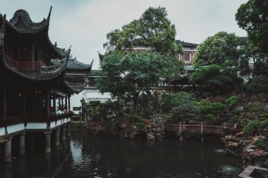 Şangay, Çin - Haziran 06, 2024: Karmaşık çatıları olan geleneksel bir Çin pavyonu Şangay, Yu Garden 'da sakin bir göletin üzerinde duruyor. Göletin yüzeyi bozulmamış, çevredeki yeşilliği ve gökyüzünü yansıtıyor..