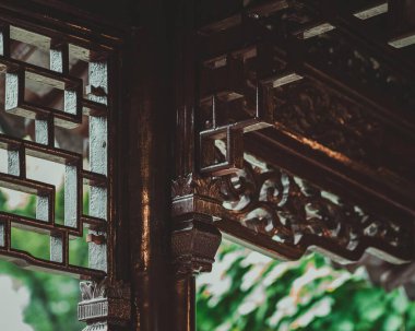 Karmaşık ahşap kafes işçiliğinin yakın plan görüntüsü ve Yu Garden, Şangay, Çin 'deki bir pavyon çatısına oyulmuş detaylar. Koyu renk ahşap, kafesin içinden görünen parlak yeşil yaprakla çelişiyor..