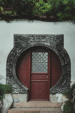 Süslü taş çerçeveli ve kırmızı ahşap kapılı geleneksel bir Çin geçidi. Kapıda geometrik bir pencere ve karmaşık oymalar var..