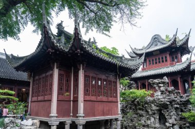 Şangay, Çin - Haziran 06, 2024: Yu Garden, Şangay 'da süslü ahşap oymalar ve kırmızı pencereli geleneksel bir Çin pavyonu bulunuyor. Bahçede kaya oluşumları ve yemyeşil yeşermeler var..