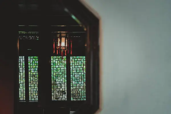 stock image A glimpse into a traditional Chinese garden, captured through a window with intricate latticework. Light streams through the lattice, illuminating the lush greenery beyond.