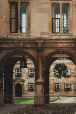 İki kemerli geçit Cambridge, İngiltere 'de bir kaldırım taşı avlusuna çıkıyor. Binanın taş cephesi pencereler ve çiçek sepetleriyle süslenmiş..