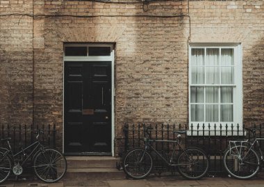 Cambridge, İngiltere 'de siyah kapısı ve penceresi olan, önünde bisikletleri olan bir tuğla bina..