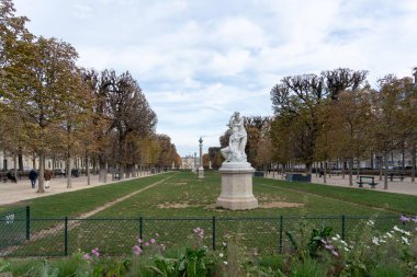 Paris, Fransa - 18 Ekim 2023: Paris, Fransa 'da her iki tarafında da sıra sıra ağaçlar olan çimenli bir parkta beyaz bir heykel duruyor.