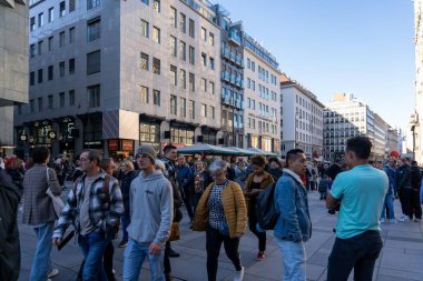 Wien, Avusturya - 28 Ekim 2023: Viyana, Avusturya 'da kalabalık bir sokak sahnesi, insanların dükkanların ve kafelerin önünden geçtiği. Binaların modern bir mimari tarzı var..