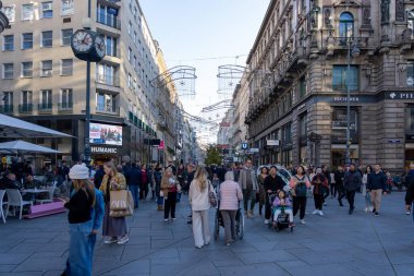 Wien, Avusturya - 28 Ekim 2023: Avusturya 'nın Viyana şehrinde kalabalık bir cadde, dükkanların ve kafelerin önünden geçen insanlar. Binalar uzun ve süslü, gökyüzü açık ve mavi..