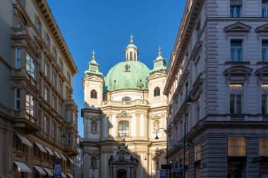 Wien, Avusturya - 28 Ekim 2023: Yeşil kubbeli bir kilise Wien, Avusturya 'da iki süslü bina arasında yer alır. Öğleden sonra güneşi sokağın karşısına uzun gölgeler bırakır..