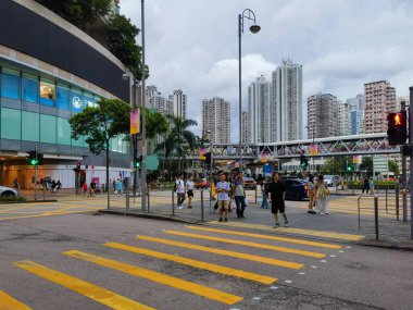 Hong Kong, Çin - 21 Temmuz 2024: Yayalar bulutlu bir gökyüzünün altında Çin 'in Hong Kong şehrinde karşıdan karşıya geçiyorlar. Sokak boyunca uzanan uzun binalar..