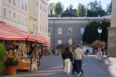 Salzburg, Avusturya - 01 Kasım 2023: Salzburg, Avusturya 'da kaldırımlı bir cadde, insanların geçtiği dükkanlar ve tarihi bir bina.