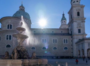 Salzburg, Avusturya - 01 Kasım 2023: Güneşin gökyüzünde parladığı Salzburg Katedrali önünde bir çeşme.