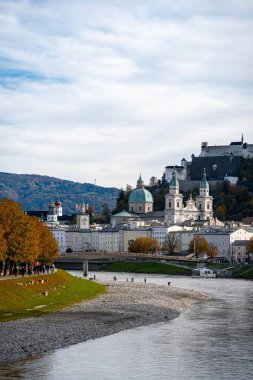 Salzburg, Avusturya - 01 Kasım 2023: Salzburg, Avusturya 'dan bir nehir akmakta, ön planda yaya köprüsü ve arka planda bir tepe kalesi bulunmaktadır.