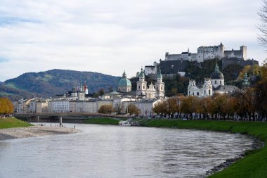 Salzburg, Avusturya - 01 Kasım 2023: Avusturya 'nın Salzburg kentinden geçen bir nehir, kente bakan bir tepenin üzerine tünemiş bir kaleye sahiptir..