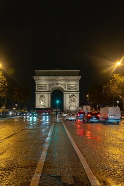 Paris, Fransa - 19 Ekim 2023: Paris, Fransa 'daki Zafer Takı, ıslak kaldırım taşından geçen arabalarla gece aydınlandı.