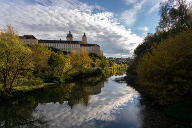 Melk, Avusturya - 25 Ekim 2023: Avusturya 'nın Melk kentindeki bir nehrin sakin sularına yansıyan büyük bir binanın manzarası.