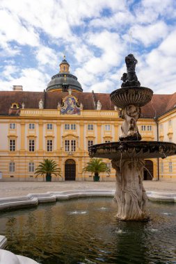 Melk, Avusturya - 25 Ekim 2023: Avusturya 'nın Melk kentindeki sarı bir binanın önündeki havuza dökülen taştan bir çeşme.