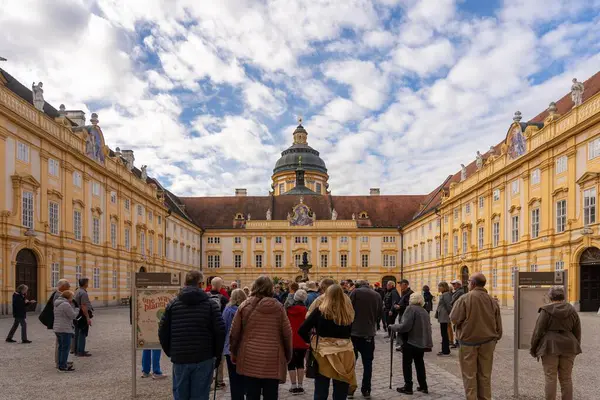 stock image Melk, Austria - October 25, 2023 : A large group of tourists gather in the courtyard of a monastery in Melk, Austria. The building has a yellow facade and a dome.