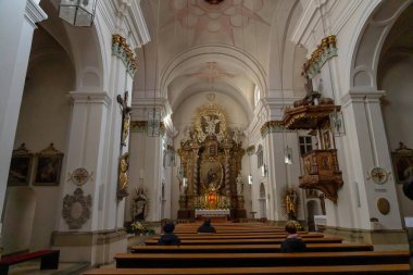 Almanya - 06 Kasım 2023: Beyaz duvarları, ahşap sıraları ve altın yapraklı sunağı olan bir kilise.