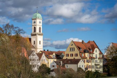 Regensburg, Almanya - 06 Kasım 2023: Regensburg, Almanya 'da renkli evlerin üzerinde bir saat kulesi duruyor. Mavi bir gökyüzü ve kabarık bulutlar çatıyı gözetliyor..
