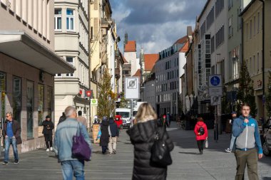 Regensburg, Almanya - 06 Kasım 2023: İnsanlar Almanya 'nın Regensburg kentinde yüksek binalarla çevrili bir kaldırım taşı caddesinde yürüyor.