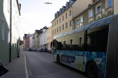 Regensburg, Almanya - 06 Kasım 2023: Regensburg, Almanya 'da binalarla dolu dar bir caddeden mavi bir otobüs geçiyor.