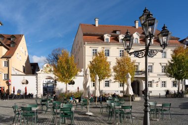 Regensburg, Almanya - 06 Kasım 2023: Regensburg, Almanya 'da yeşil sandalyeli ve masalı bir kaldırım taşı meydanı, ve ön planda bir sokak lambası.