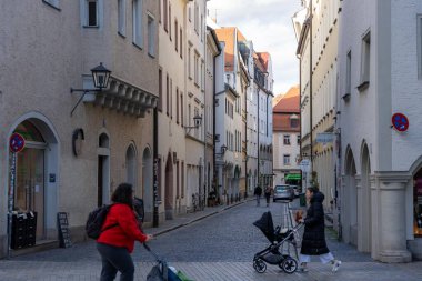 Regensburg, Almanya - 06 Kasım 2023: Regensburg, Almanya 'da tarihi binalarla dolu dar bir kaldırım. Bir kadın bebek arabasını diğer bir kadının yanından itiyor. Ters yönde yürüyor..