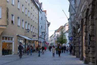 Regensburg, Almanya - 06 Kasım 2023: Regensburg, Almanya 'da tarihi binalarla dolu bir kaldırım taşı caddesi, insanlarla dolup taşıyor ve yalnız bir bisikletçi.
