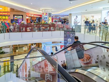 Shenzhen, Çin - 29 Temmuz 2024: Bir adam Shenzhen, Çin 'deki parlak ve modern bir alışveriş merkezinde yürüyen merdivene biniyor.