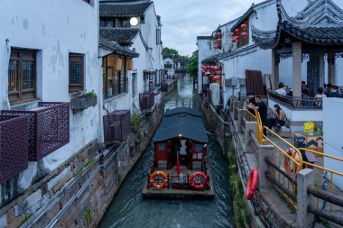 Suzhou, Çin - 10 Haziran 2024: Çin 'in Suzhou şehrinde küçük bir tekne suda yüzüyor. Kanal beyaz binalar ve geleneksel Çin mimarisi ile kaplı..