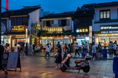 Suzhou, Çin - 10 Haziran 2024: Çin 'in Suzhou şehrinde geleneksel mimarisi ve aydınlatılmış vitrinleri olan hareketli bir gece pazarı. İnsanlar kaldırımda yürüyor, manzaranın ve seslerin tadını çıkarıyorlar..