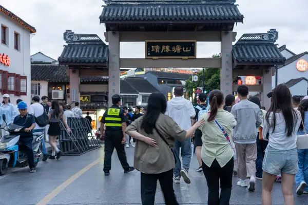 stock image suzhou, China - June 10, 2024 : Pedestrians walk through an ornate gateway in Suzhou, China.  The traditional architecture and bustling street create a vibrant scene.