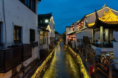 suzhou, China - June 10, 2024 : A canal runs through the heart of Suzhou, China, illuminated by lanterns strung across the water.  The buildings along the canal are old and traditional, with intricate details and ornate roofs. clipart