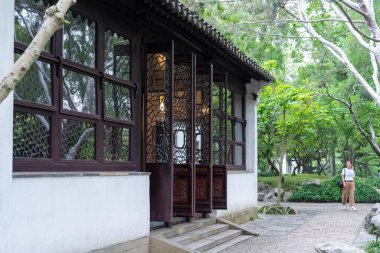 Suzhou, Çin - 11 Haziran 2024: Beyaz bir duvarı ve gür yeşilliklerle çevrili ahşap kapılı geleneksel bir Çin bahçe binası.