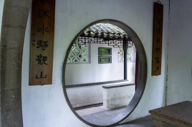 Suzhou, Çin - 11 Haziran 2024: Çerçevelenmiş kiremit çatılı beyaz duvarlı Çin bahçesinde dairesel bir kapı.