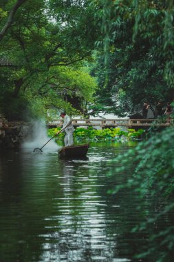 Suzhou, Çin - 11 Haziran 2024: Bir adam Çin 'in Suzhou kentindeki mütevazı yönetimin bahçesinde sakin bir gölette kürek çekiyor..