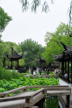Suzhou, Çin - 11 Haziran 2024: Arka planda nilüfer yaprakları ve geleneksel Çin pavyonu olan bir göletin üzerindeki taş köprü. Çin Suzhou 'daki Mütevazı Yöneticinin Bahçesi.