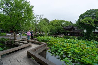 Suzhou, Çin - 11 Haziran 2024: Çin 'in Suzhou kentindeki mütevazı yönetimin bahçesinde bir nilüfer yaprağı göleti boyunca uzanan taş köprü.