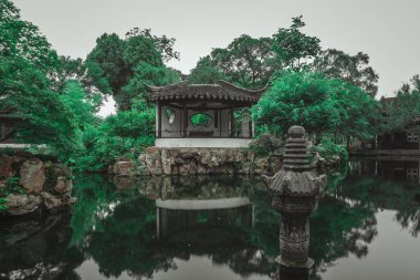 Geleneksel bir Çin bahçe pavyonu durgun bir gölete bakan kayalık bir çıkıntıda bulunur..