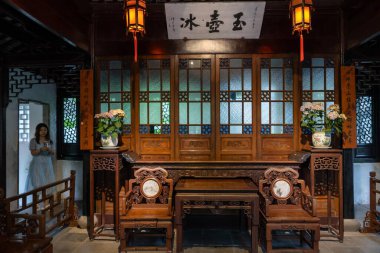 Suzhou, Çin - 11 Haziran 2024: Ahşap mobilyalar, süslü oymalar ve pencereden bahçe manzaralı geleneksel bir Çin iç mimarisi.