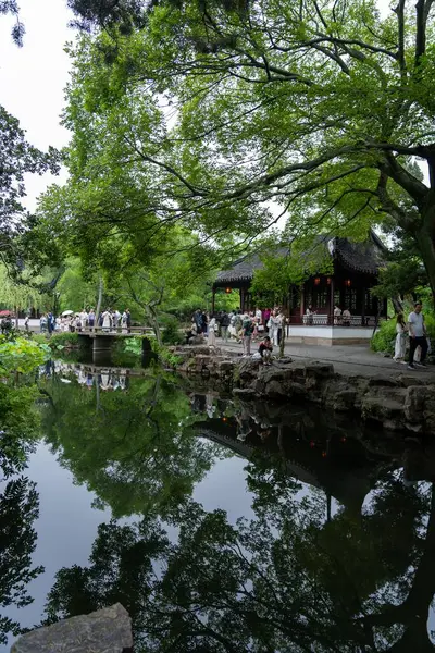 stock image Suzhou, China - June 11, 2024 : A tranquil pond reflects lush greenery and a traditional Chinese pavilion, with visitors enjoying the serene setting.