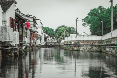 Beyaz duvarları, taş bir köprüsü ve yemyeşil ağaçları olan geleneksel bir Çin köyünün içinden bir kanal geçiyor..