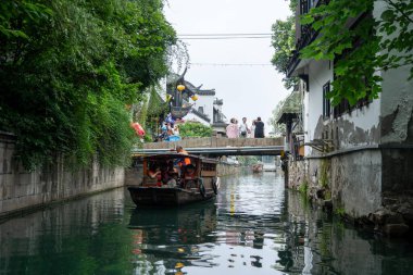 Suzhou, Çin - 11 Haziran 2024: Küçük ahşap bir tekne Çin 'in Suzhou kentindeki dar bir kanalda yol alır. Kanal geleneksel Çin binaları ve bereketli yeşilliklerle kaplı..