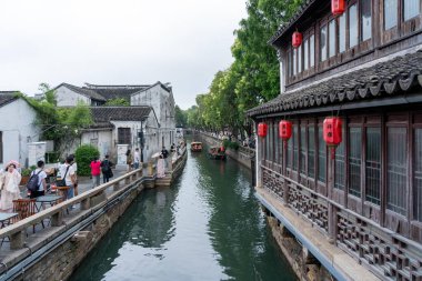 Suzhou, Çin - 11 Haziran 2024: Geleneksel binalar ve yayalarla dolu bir Çin köyü boyunca dar bir kanal akıyor.