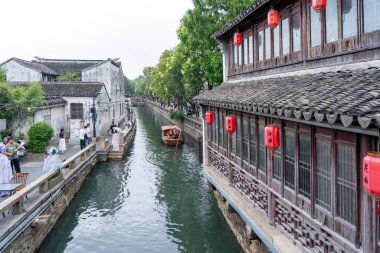 Suzhou, Çin - 11 Haziran 2024: Geleneksel bir Çin kasabasından bir kanal akıyor, tarihi binalarla dolu, kıyılarda yürüyen insanlar ve su yolundan geçen yolcularla dolu bir tekne..