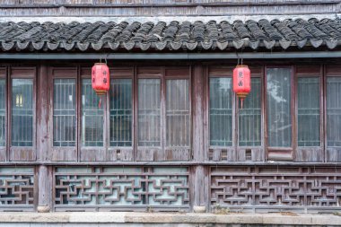 Suzhou, Çin - 11 Haziran 2024: Kırmızı fenerler Çin 'in Suzhou kentindeki antik bir ahşap binanın saçağında asılı duruyor. Binada karmaşık kafes ve fayanslı çatı da dahil olmak üzere geleneksel Çin mimarisi yer alıyor..