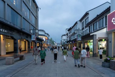 Suzhou, Çin - 11 Haziran 2024: Çin 'in Suzhou şehrinde bulutlu bir gökyüzü altında modern mağazaların önünden geçen kalabalık bir alışveriş caddesi.