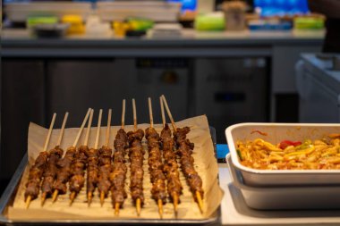 Suzhou, Çin - 11 Haziran 2024: Ahşap çubuklarda ızgara et şişleri kırmızı ve yeşil biberli beyaz seramik yemek tabağının yanında kahverengi metal bir tepside oturur..