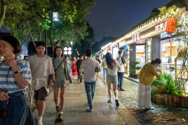 Suzhou, Çin - 11 Haziran 2024: Çin 'in Suzhou şehrinde hareketli bir gece caddesi, parlak ışıklı dükkanların ve geleneksel mimarinin önünden geçen insanlar.