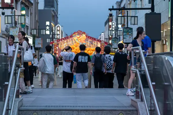 stock image Suzhou, China - June 11, 2024 : People walk down a city street in Suzhou, China, past shops and streetlights.